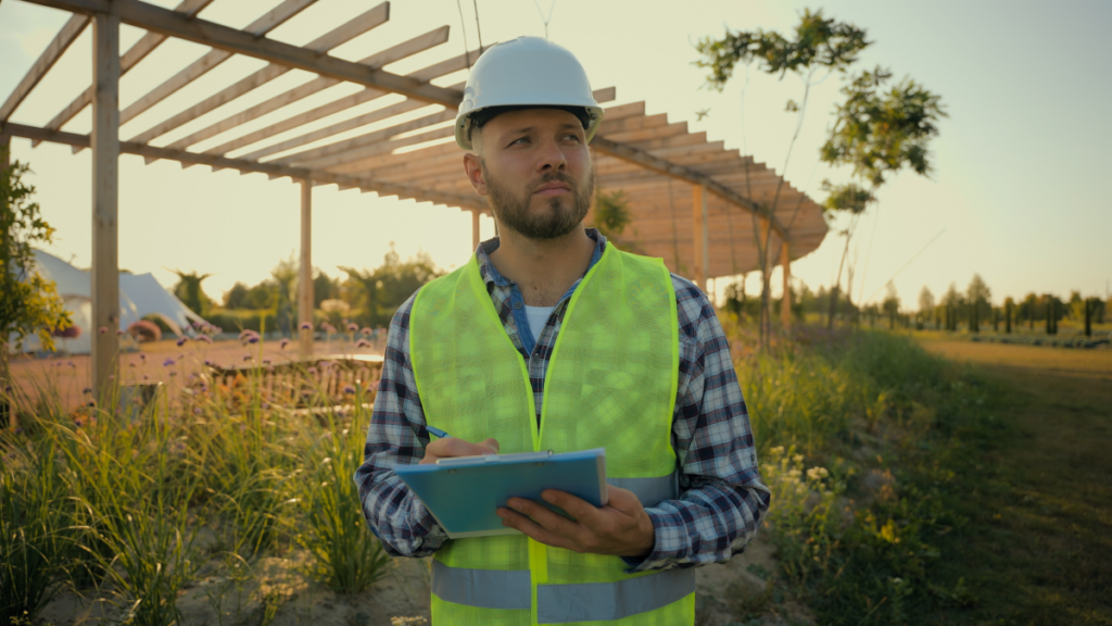 Homem usando capacete de obra fazendo anotações em um jardim. Arquitetura