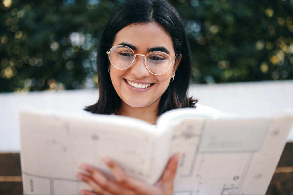Mulher de óculos e sorrindo olhando para um livro de arquitetura.