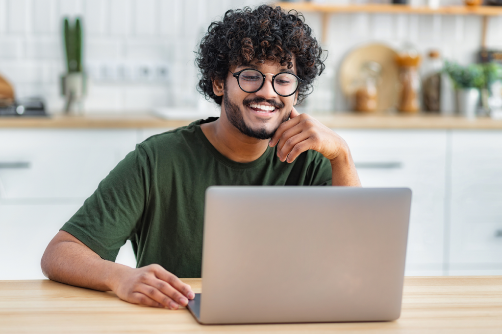 Homem usa computador na sua cozinha e sorri. ead comercio exterior.