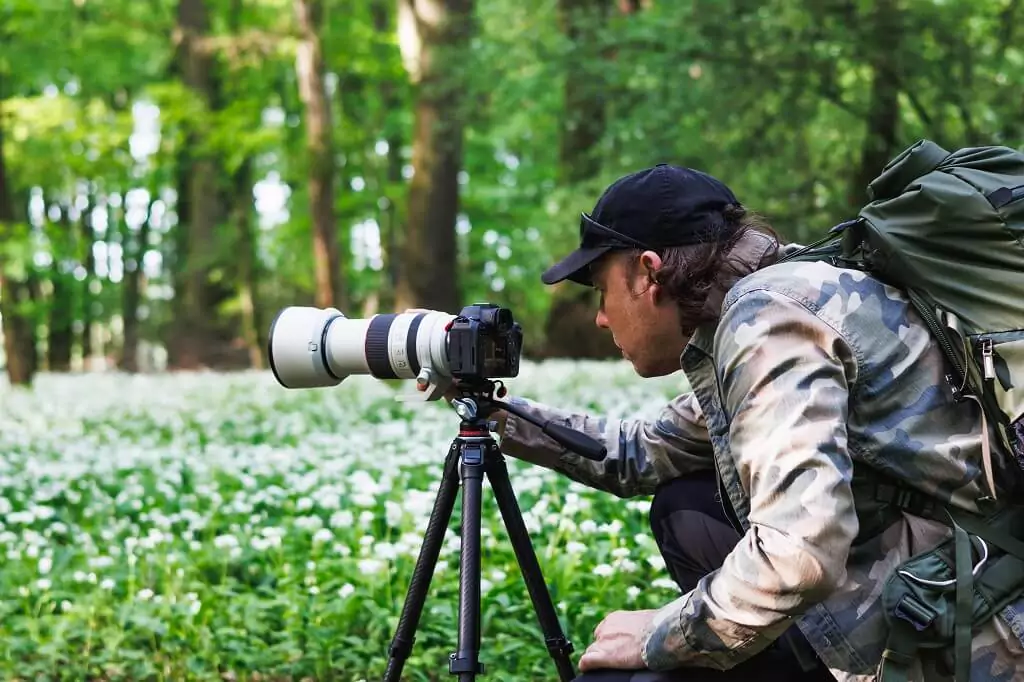 fotografo em campo de flores ajustando câmera