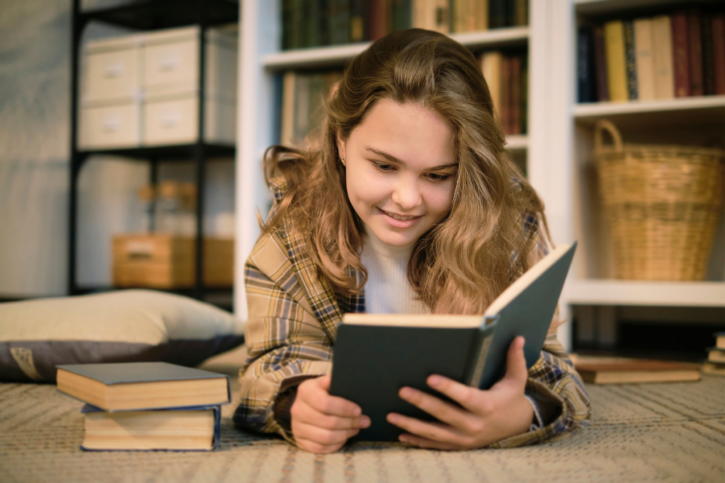 Menina lendo livro deitada no chão da sala.